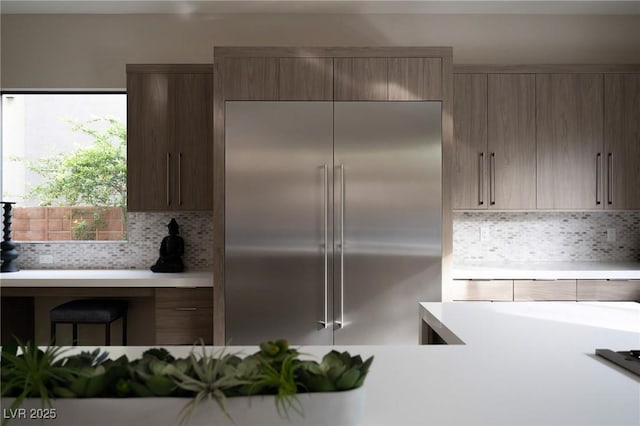 kitchen with light countertops, modern cabinets, decorative backsplash, and built in fridge