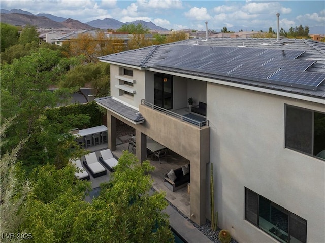 rear view of property with solar panels, a balcony, stucco siding, and a mountain view
