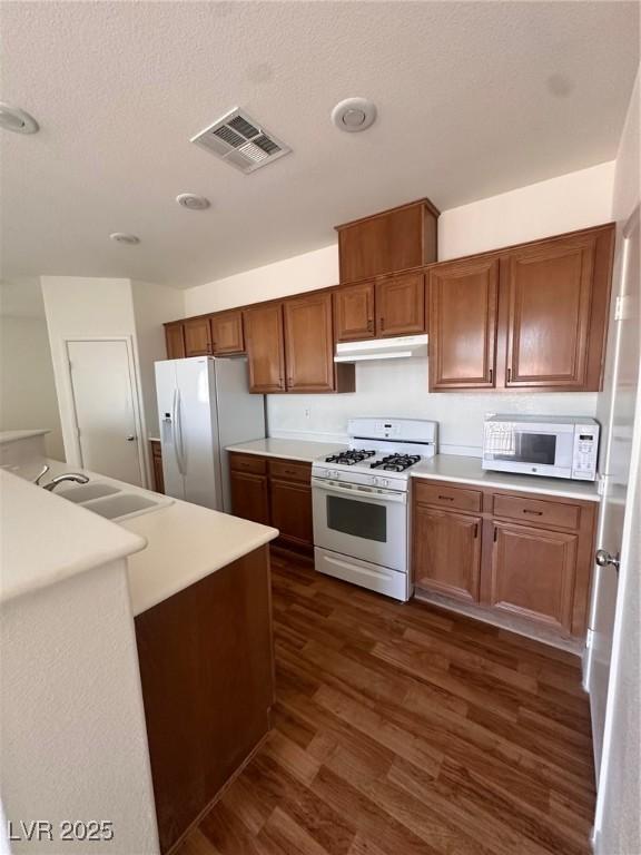 kitchen featuring brown cabinets, white appliances, under cabinet range hood, dark wood-type flooring, and visible vents
