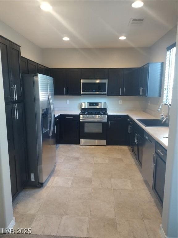 kitchen with appliances with stainless steel finishes, a sink, light countertops, recessed lighting, and dark cabinets