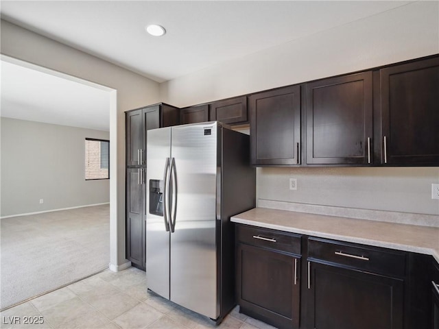 kitchen featuring stainless steel refrigerator with ice dispenser, light carpet, light countertops, dark brown cabinetry, and baseboards