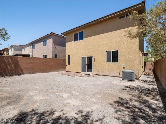 rear view of property featuring stucco siding, central AC unit, and a fenced backyard