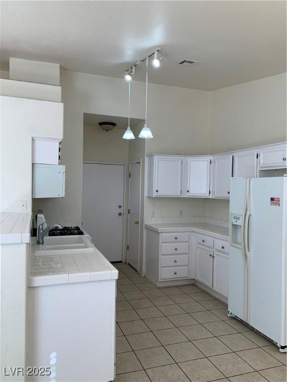 kitchen featuring white cabinets, tile countertops, light tile patterned floors, a sink, and white refrigerator with ice dispenser