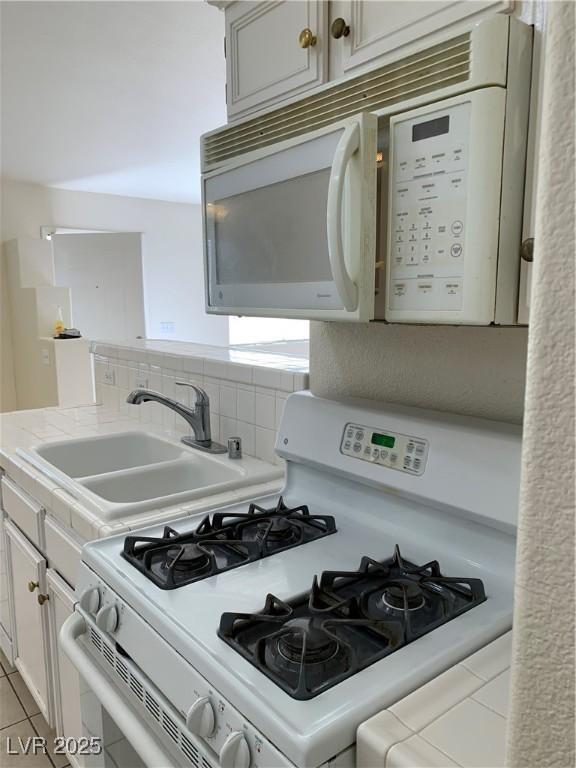 kitchen with a sink, white appliances, light tile patterned floors, light countertops, and backsplash
