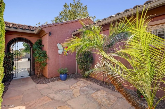 view of exterior entry with a tile roof, a gate, and stucco siding