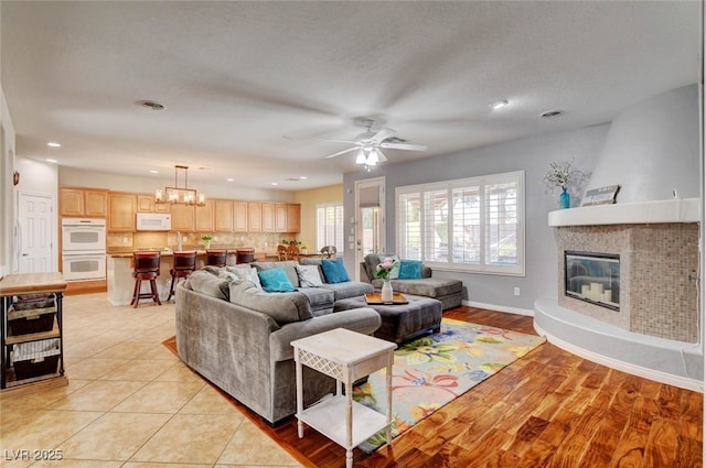 living room with recessed lighting, visible vents, baseboards, a fireplace, and ceiling fan with notable chandelier