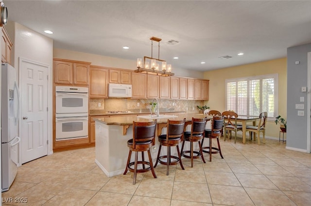 kitchen featuring tasteful backsplash, a kitchen breakfast bar, white appliances, and light tile patterned floors