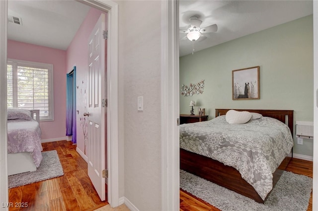 bedroom with baseboards, a ceiling fan, wood finished floors, and visible vents