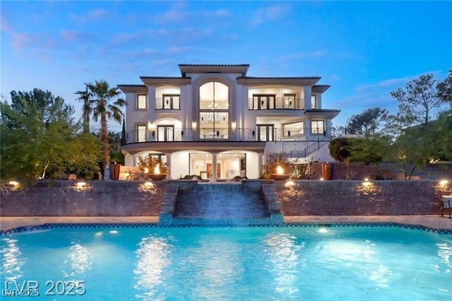 rear view of property with fence, a fenced in pool, a balcony, and stucco siding