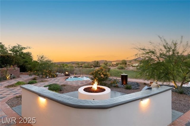 patio terrace at dusk featuring an outdoor fire pit and fence