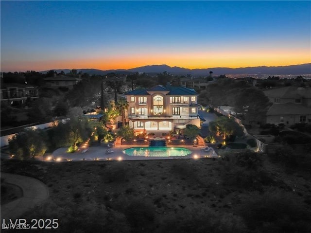 back of property at dusk with an outdoor pool, a balcony, a mountain view, and a patio