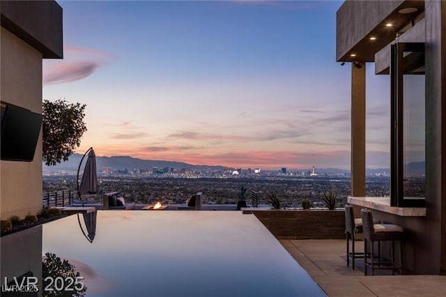 pool at dusk featuring a view of city, outdoor dry bar, and an outdoor fire pit