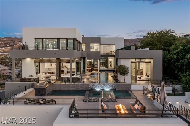 back of house with a balcony, an outdoor living space with a fire pit, a patio, stucco siding, and a pool with connected hot tub