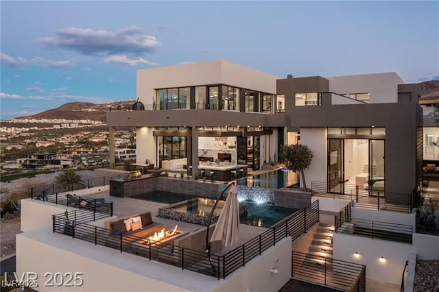 rear view of property featuring a mountain view, an in ground hot tub, an outdoor living space with a fire pit, an infinity pool, and a patio area