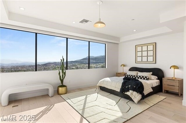 bedroom with visible vents, a tray ceiling, light wood-style floors, and a mountain view