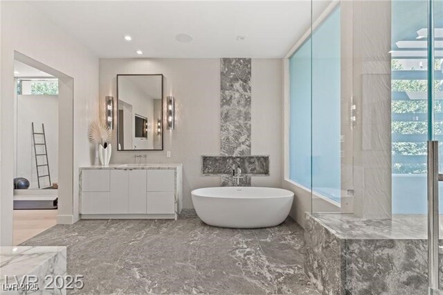 full bath with marble finish floor, a freestanding tub, vanity, and a wealth of natural light