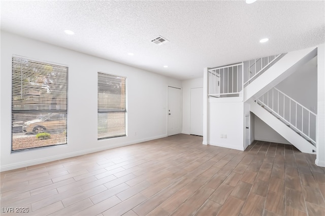 unfurnished living room with stairs, a textured ceiling, visible vents, and recessed lighting