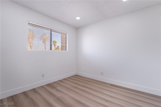empty room with recessed lighting, light wood-style floors, a textured ceiling, and baseboards