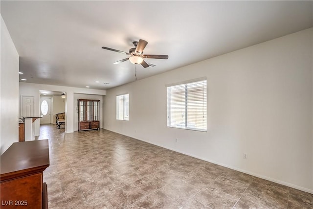 unfurnished living room featuring a wealth of natural light, a ceiling fan, and baseboards