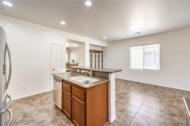 kitchen featuring a sink, brown cabinets, a kitchen island with sink, baseboards, and appliances with stainless steel finishes