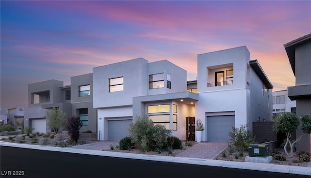 modern home with an attached garage, driveway, a balcony, and stucco siding