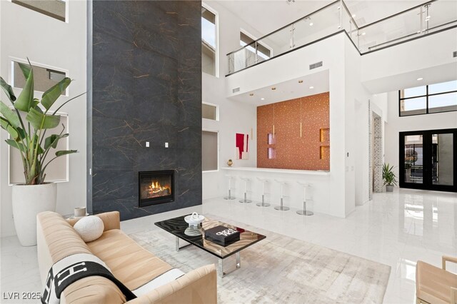living area featuring a high ceiling, marble finish floor, a wainscoted wall, a high end fireplace, and visible vents