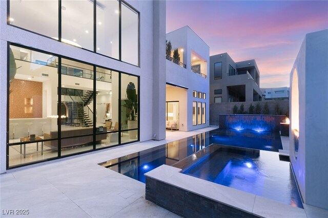 pool at dusk featuring a patio, a fenced in pool, and an in ground hot tub