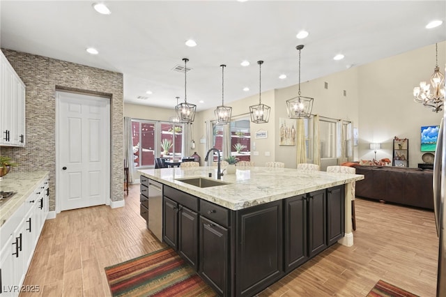 kitchen with stainless steel dishwasher, a sink, white cabinetry, light wood-style flooring, and a notable chandelier