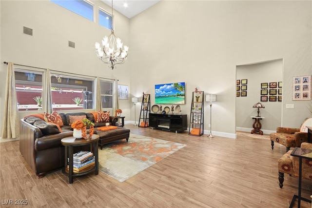 living area with visible vents, baseboards, a towering ceiling, light wood-style floors, and a chandelier