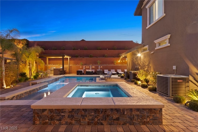 pool at dusk featuring central air condition unit, a patio area, and an in ground hot tub