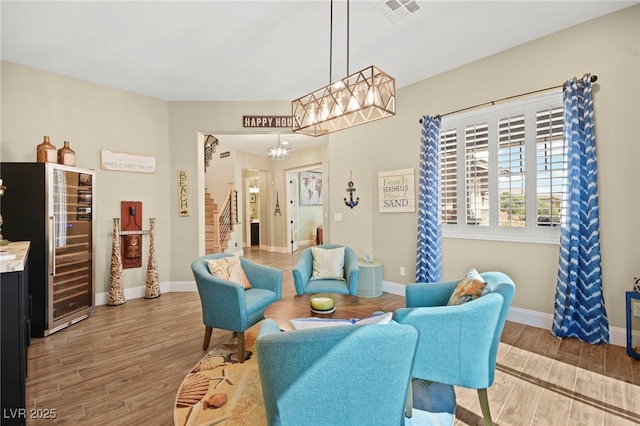interior space featuring beverage cooler, an inviting chandelier, wood finished floors, visible vents, and stairs