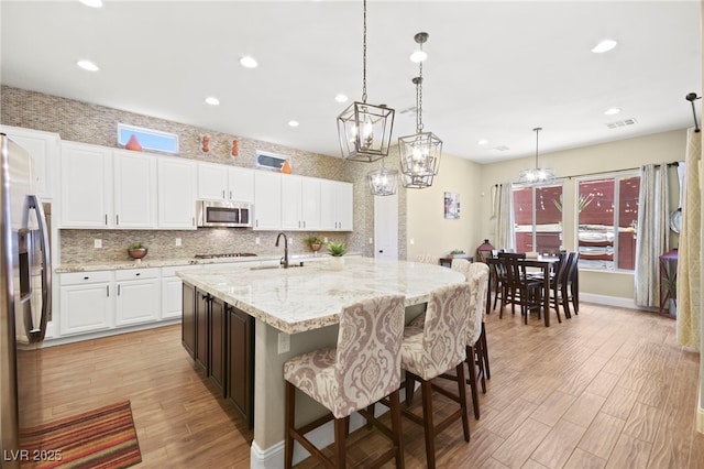 kitchen featuring a sink, a kitchen island with sink, light wood-type flooring, stainless steel appliances, and white cabinetry