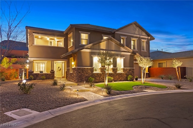 view of front of home featuring stucco siding, stone siding, a balcony, and fence