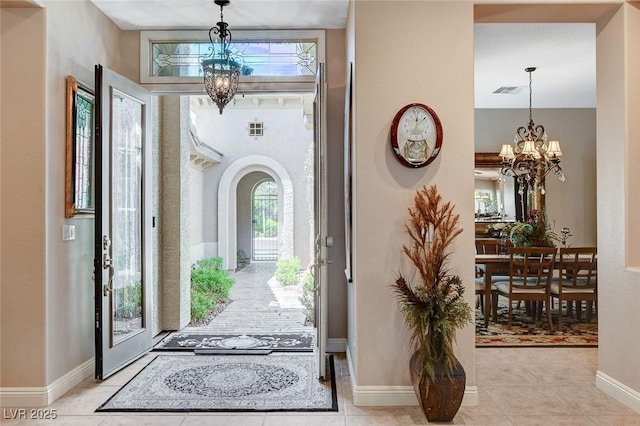 foyer entrance featuring an inviting chandelier, visible vents, light tile patterned floors, arched walkways, and baseboards