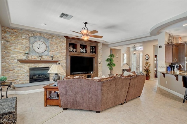 living area with a stone fireplace, visible vents, ceiling fan, and light tile patterned floors