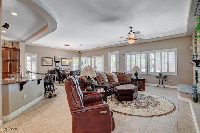 living area with baseboards, a ceiling fan, light tile patterned flooring, and a raised ceiling