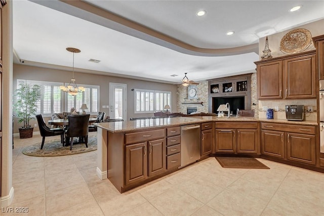 kitchen with a peninsula, light tile patterned flooring, a chandelier, dishwasher, and a stone fireplace