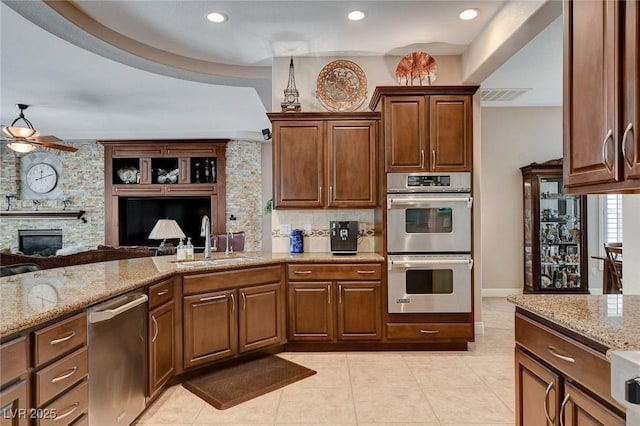 kitchen with light stone counters, a ceiling fan, appliances with stainless steel finishes, and a sink
