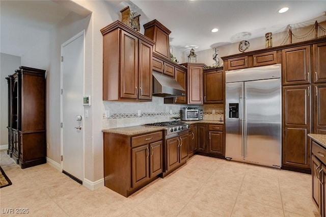 kitchen with stainless steel appliances, recessed lighting, decorative backsplash, light stone countertops, and under cabinet range hood