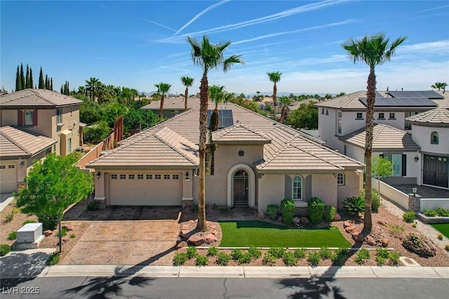 mediterranean / spanish-style home with a tile roof, decorative driveway, a garage, stucco siding, and a residential view