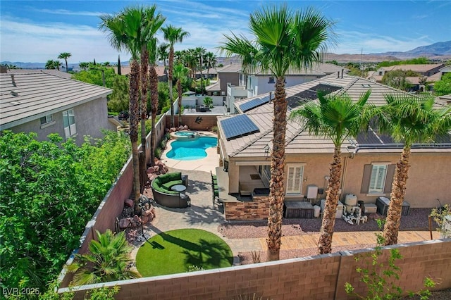 rear view of property with a fenced backyard, a mountain view, roof mounted solar panels, a patio, and stucco siding