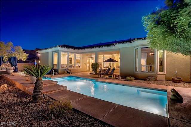 4624 Leon De Oro Dr, Las Vegas, NV 89129 - back of house at night featuring stucco siding, a patio, an outdoor pool, and roof mounted solar panels