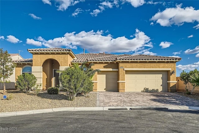 mediterranean / spanish home with stucco siding, an attached garage, decorative driveway, and a tiled roof
