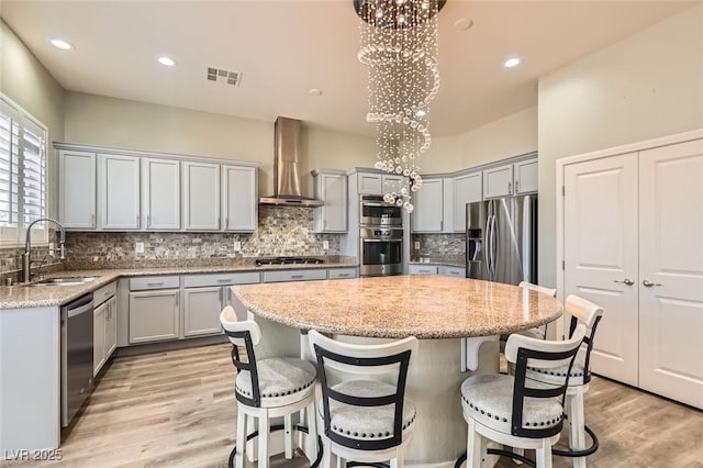 kitchen with wall chimney range hood, a sink, gray cabinets, stainless steel appliances, and a kitchen island