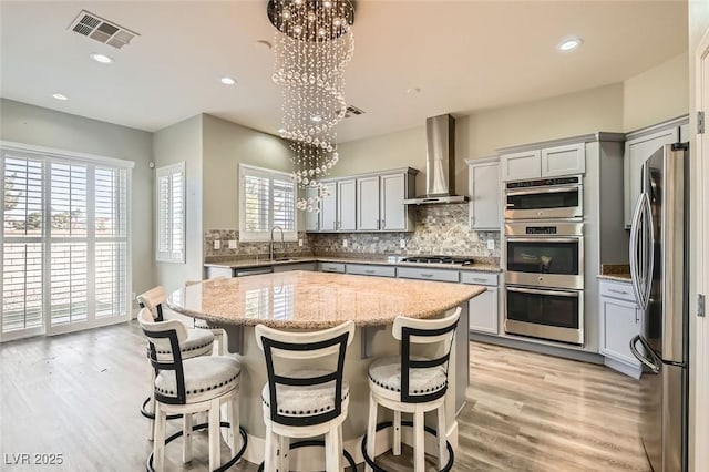 kitchen with wall chimney exhaust hood, stainless steel appliances, visible vents, and gray cabinets