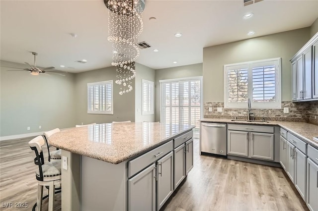 kitchen with stainless steel dishwasher, a sink, ceiling fan with notable chandelier, gray cabinetry, and a kitchen island