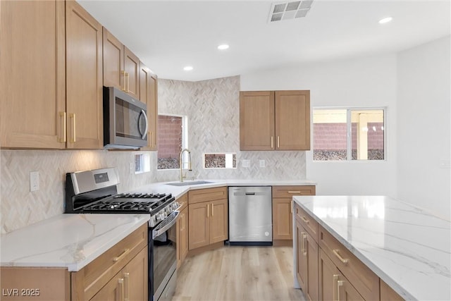 kitchen featuring light wood finished floors, a sink, visible vents, light stone counters, and appliances with stainless steel finishes