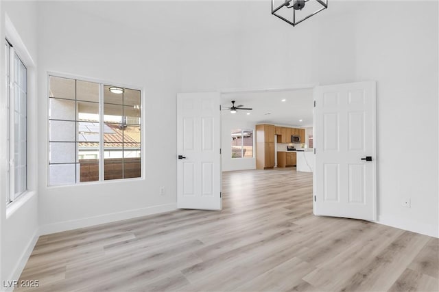 interior space featuring a ceiling fan, a high ceiling, light wood-style flooring, and plenty of natural light