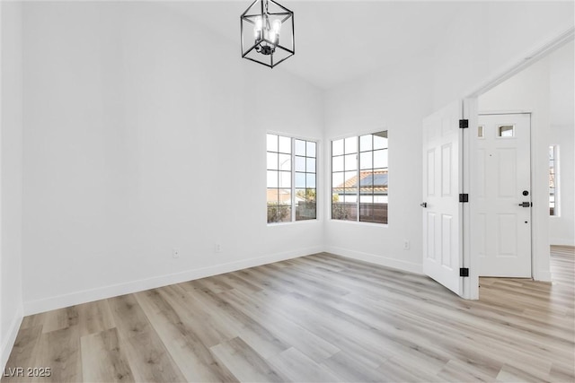 unfurnished dining area featuring light wood-type flooring, a towering ceiling, baseboards, and a notable chandelier
