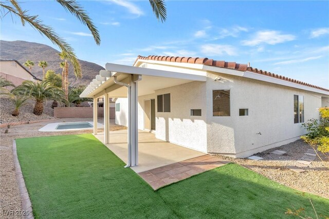 rear view of property featuring a patio area, a tiled roof, a mountain view, a yard, and stucco siding